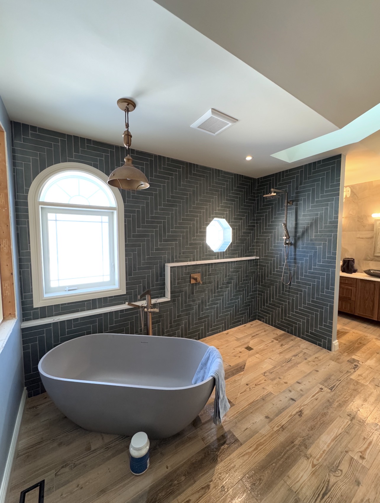 Luxury primary bathroom with dark blue-grey herringbone tile walls and freestanding tub